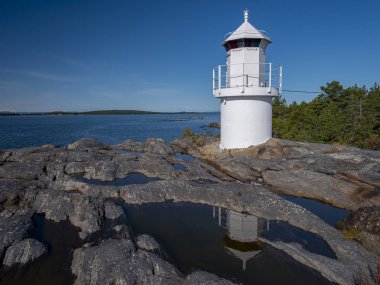 Bulutsuz gökyüzüne karşı kayalık sahilde beyaz bir deniz feneri manzarası