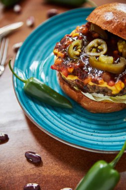 Yağlı hamburgerli tabak ve etli peynir ve ahşap masada yeşil biber, yakın görüş, fast food konsepti 