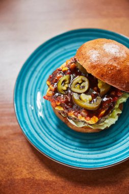 Yağlı hamburgerli tabak ve etli peynir ve ahşap masada yeşil biber, yakın görüş, fast food konsepti 