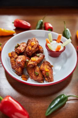 Kızarmış tavuk kanatlı tabak ve ahşap masada biberli kase, yakın görüş.