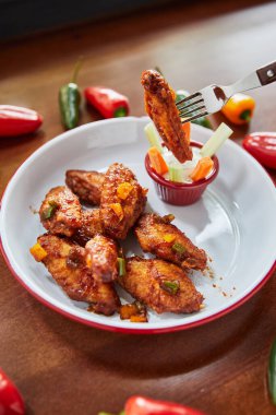Kızarmış tavuk kanatlı çatal ve soslu tabak ve ahşap masada biber, yakın görüş.