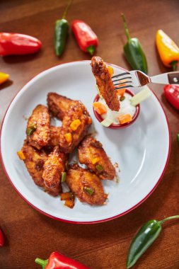 Kızarmış tavuk kanatlı çatal ve soslu tabak ve ahşap masada biber, yakın görüş.