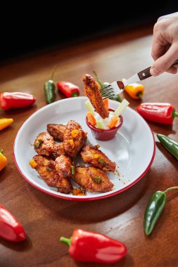 Erkek eli çatallı, kızarmış tavuk kanatlı, soslu ve ahşap masada biberli, yakın görüşlü.