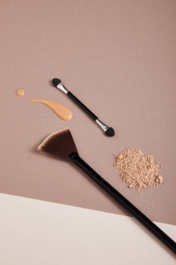 Profesyonel makyaj fırçasına sahip toz ve bej arka planda fondöten damlaları, yakın görüş, güzellik konsepti 
