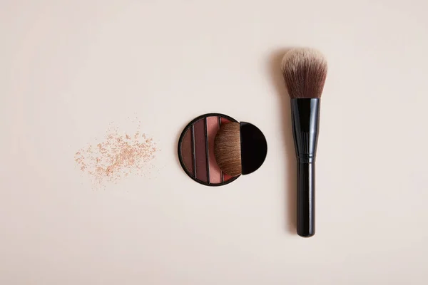 eyeshadows with professional face makeup brushes on beige background, close view, beauty concept