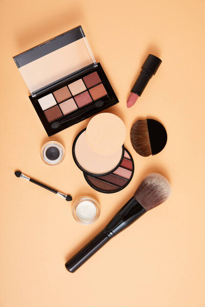 порошок с профессиональными кисточками для макияжа и тенями для век с помадой на бежевом фоне, близкий вид, концепция красоты
 