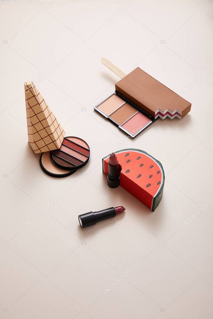 powder with eyeshadows and decorative ice-cream with lipsticks on beige background, close view, beauty concept 