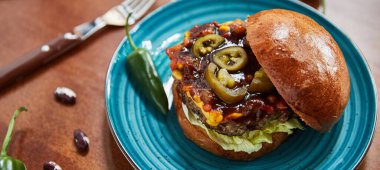 Yağlı hamburgerli tabak ve etli peynir ve ahşap masada yeşil biber, yakın görüş, fast food konsepti 