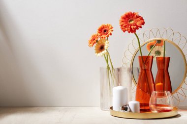 Şık bir ayna, cam ve vazolarla mumlar, ahşap yüzey üzerinde gerbera çiçekleri, ışık odası, yakın görüş.