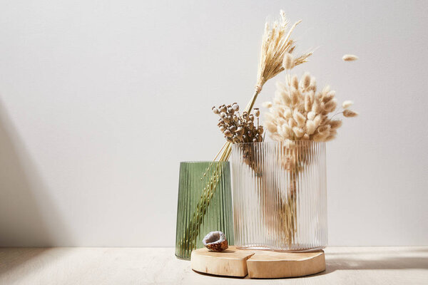 glass vases with decorative spikelets on wooden surface in light room, close view