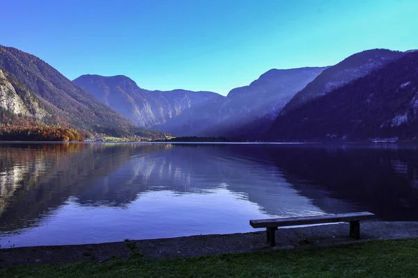 Beautiful Austrian landscape with a romantic bench on Hallstatt lake shore with blue sky and mountains