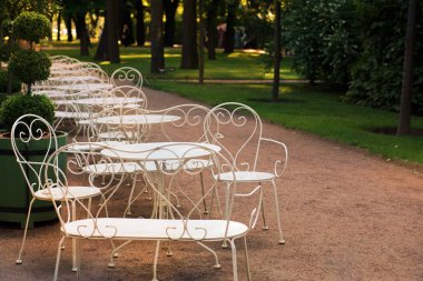 Zarif beyaz masa ve sandalye bir yaz akşamı bahçesinde boş Kafe ziyaretçiler için bekliyor.
