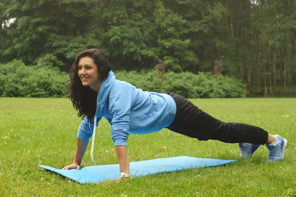 Girl physical education teacher shows exercise push-up in the park on a summer morning.