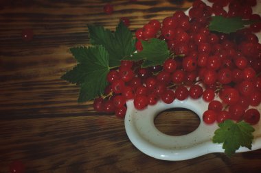 Ahşap bir masa, boğuk ışık üzerinde bir beyaz tahta üzerinde yapraklar ile Olgun kırmızı kuş üzümü.