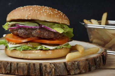 Büyük hamburger eti kızarmış pirzola, domates, salatalık turşusu, peynir, soğan ve salata ile. Ahşap ahşap bir parça yanında patates kızartması.