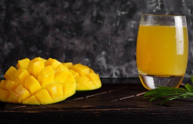 Mango ve suyu bir bardak koyu bir arka plan ile ahşap bir gemide dilimlenmiş.