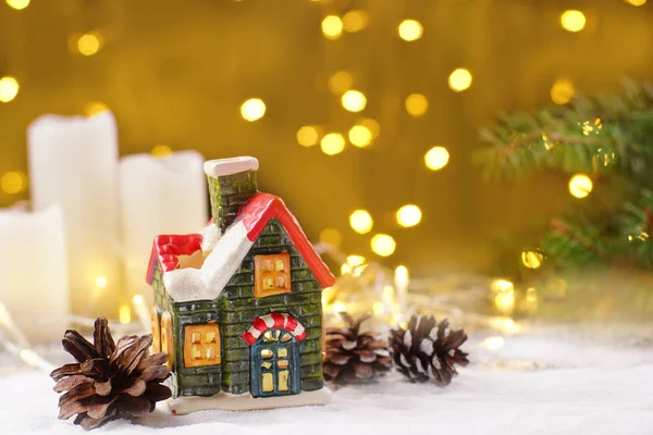 Decoração da mesa de Ano Novo na forma de uma casa de barro, velas brancas com guirlandas cintilantes em um fundo dourado — Fotografia de Stock