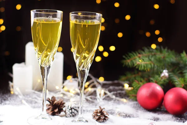 Dois copos de champanhe ou suco na mesa, decorados com uma guirlanda brilhante, bolas vermelhas, um galho de árvore de Natal e velas brancas. — Fotografia de Stock