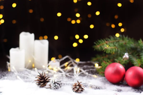 Blurred background for New Year card, dark background with glowing garland, red Christmas balls and white candles on the table