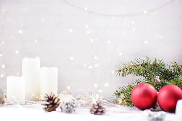 Белый фон для рождественской открытки, стена со светящимися гирляндами, красные рождественские шары и белые свечи на столе — стоковое фото