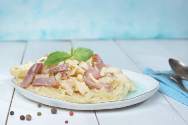 Bir ahşap beyaz masa üzerinde duran bir tabakta Fesleğenli makarna carbonara