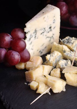 Koyu bir kayrak üzerinde farklı çeşitleri kırmızı üzüm ve peynir