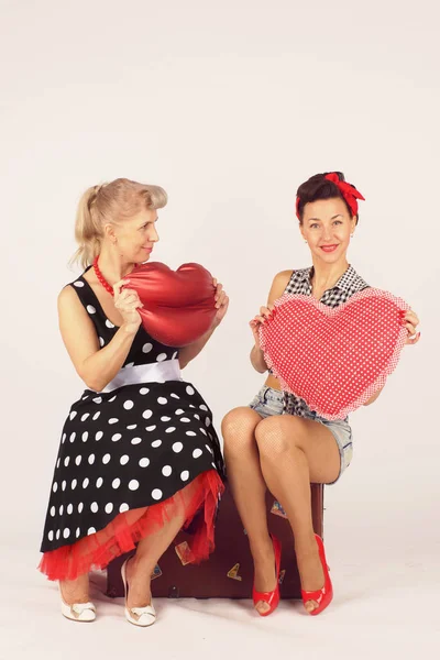 İki pinup kız bir yol bavul üzerinde oturup beyaz bir arka plan üzerinde peluş kalpleri tutun