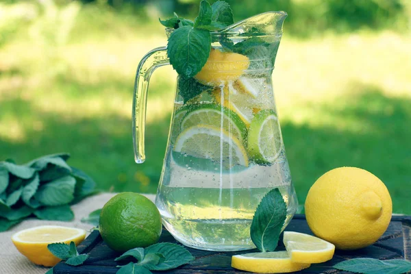 Limonádé az asztalon, a természetben, citrom és lime, amelyek darabjait használták a készítmény az ital — Stock Fotó