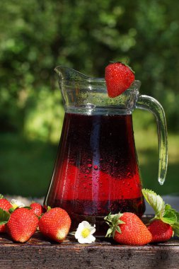 Soğuk çilek suyu ile bir sürahi, damlacıkları ile kaplı, yaprakları ile çilek yanında, sadece bahçeden aldı