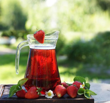 Çilek büyümek yeşil bir bahçenin arka planına karşı soğuk bir sürahi olgun çilek meyveleri doğal suyu