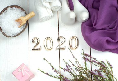 Spa seti ve altın sayılar 2020 beyaz ahşap bir tahta üzerinde mor bir bez, kuş figürleri ve bir fundalık.