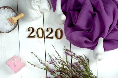 Spa seti ve altın sayılar 2020 beyaz tahta üzerinde mor bir bez ve fundalık bir filiz ile.