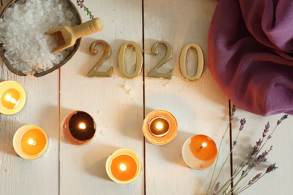 Gold numbers 2020 on a background of white boards next to sea salt for spa treatments, scented candles and a sprig of lavender lie nearby — Stock Photo, Image