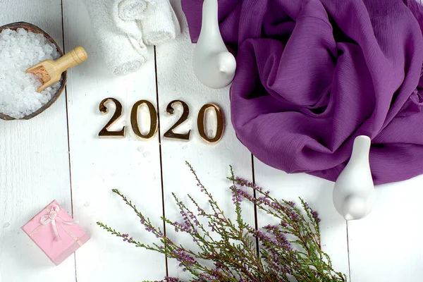 Spa seti ve altın sayılar 2020 beyaz tahta üzerinde mor bir bez ve fundalık bir filiz ile.