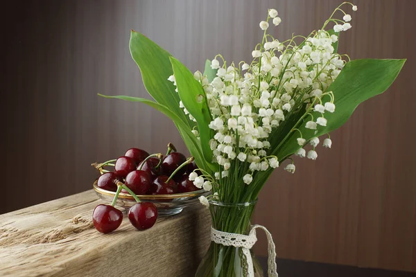 Beautiful Bouquet Lilies Valley Brown Background Standing Next Bowl Cherries — Stock Photo, Image