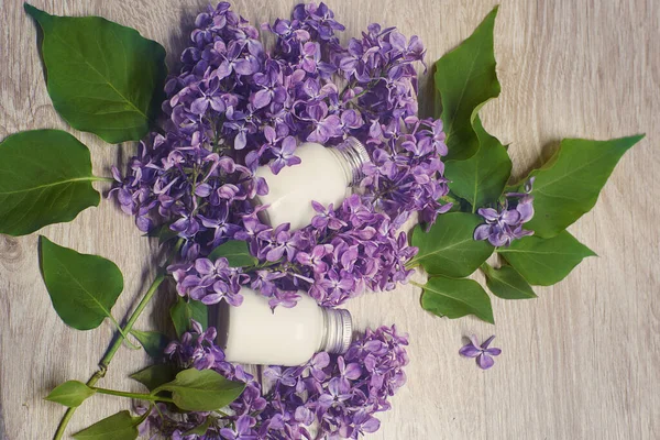 Still life with cosmetics in bottles and lilac flowers with leaves, spa concept