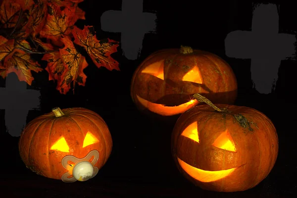 Halloween pumpkins with glowing eyes on a dark background with autumn leaves.