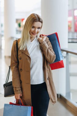Sarışın kız gülümseme ve tutun onun elleri serin shooping çantalar farklı renk - kırmızı, mavi, sarı. Konsept: alışveriş, satış, tüketim, yaşam biçimi