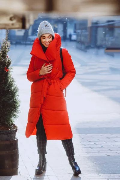 快乐的时尚女孩微笑着摆出红色的羽绒服和针织帽子 圣诞节假期概念 — 图库照片