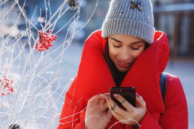 ceket ve örme gri şapka türleri metin sms veya iletinin onun hareket eden smartphone ayakta kış geleneksel Noel ağacının yanında sokak üzerinde aşağı kırmızı kış mutlu kadın portresi kapatın. Noel, yeni yıl ve kış tatil kavramı - Im