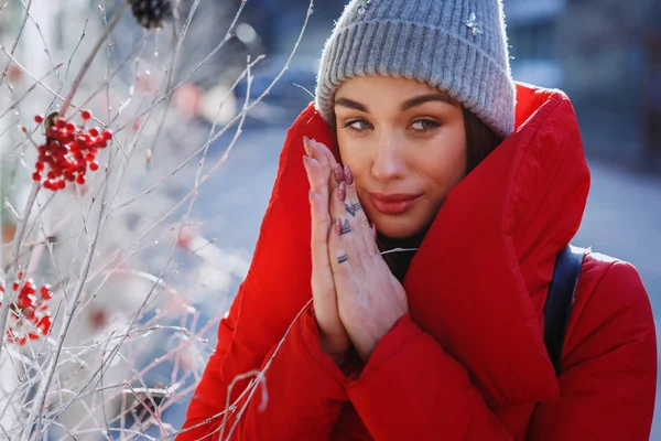 一个穿着灰色针织帽子和红色外套的迷人女孩的肖像 当她站在街上 在一个阳光明媚的冬日圣诞装饰 圣诞节 新年和寒假概念 — 图库照片