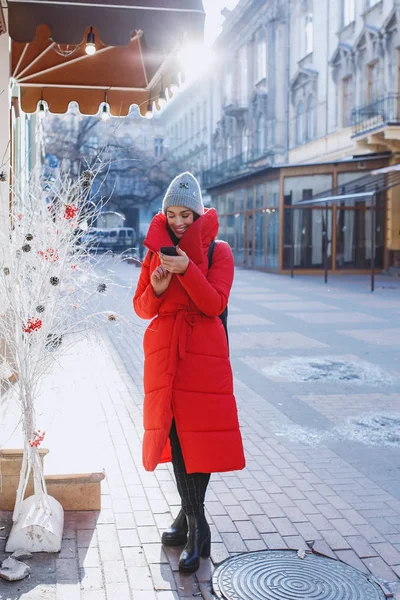在老城区的冬街里 快乐的沃南穿着红色的冬衣微笑和短信或短信给朋友 圣诞节 新年和寒假概念 — 图库照片
