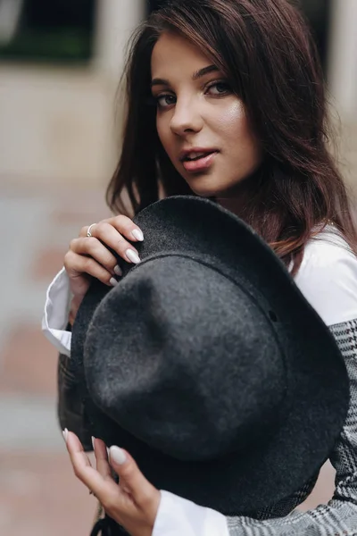 Beautiful dark-haired girl in gray jacet hold a hat on her chest — Stock Photo, Image