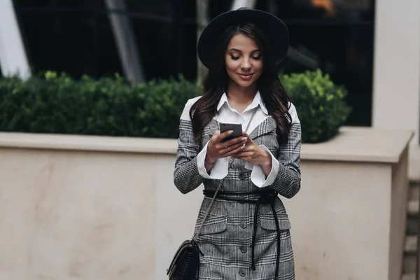 Gelukkige vrouw dragen grijze vacht en hoed met behulp van slimme telefoon in de s — Stockfoto