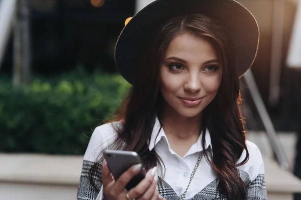 Портрет красивой женщины в современной черной шляпе смотреть в сторону с помощью мобильного телефона — стоковое фото