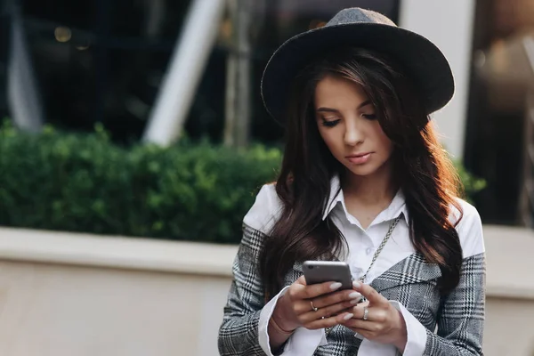 Портрет красивой женщины в современной черной шляпе с помощью смартфона, играющей в игры на мобильном телефоне — стоковое фото