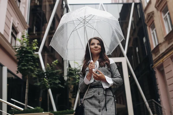 Portret van een lachende gelukkige vrouw onder een paraplu in de buurt van het oude huis, wachtend op regen. Het is lente regen. — Stockfoto