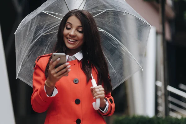 Vrouw poseren op straat met paraplu. Buiten portret van jonge glimlachende mooie vrouw spreken op mobiele telefoon, staande op straat — Stockfoto