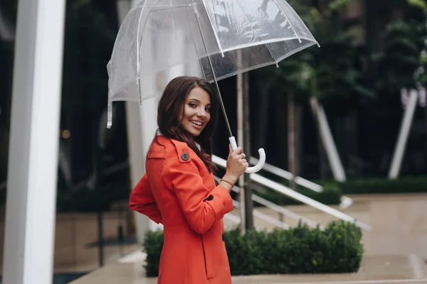 Muchacha atractiva joven elegante caminando en la calle con paraguas, día de primavera. Joven mujer de negocios europea sonriente con paraguas en la calle de la ciudad de primavera mirando a la cámara . — Foto de Stock