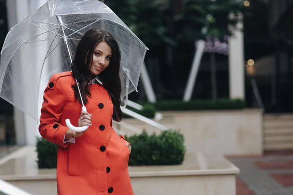 Woman portrait of young pretty girl posing at the city holding hand in pocket. Portrait of young woman in coat holding umbrella
